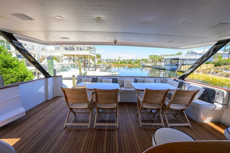 Spacious deck of 1997 Broward 108 Raised Pilothouse yacht with wooden chairs and waterfront view.