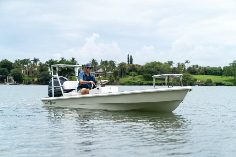 2025 BlueZones Boatworks 16' Flats boat on calm water with lush greenery in the background.