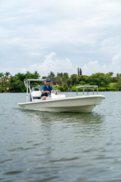 2025 BlueZones Boatworks 16' Flats boat on calm water with lush greenery in the background.