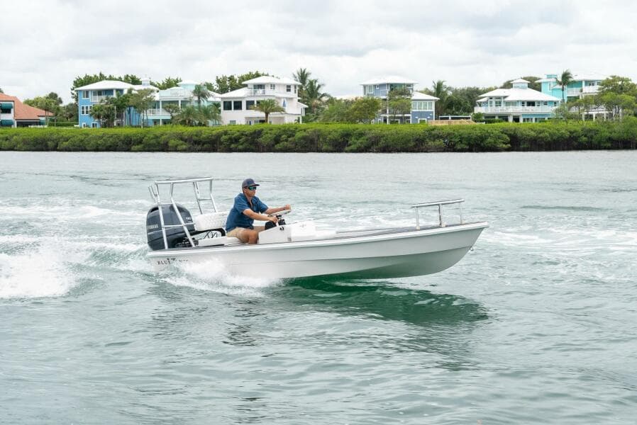 2025 BlueZones Boatworks 16' Flats cruising on water near coastal homes.
