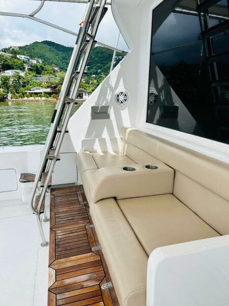 1988 Bertram 54' yacht with beige seating and wooden deck, docked by lush green hills.