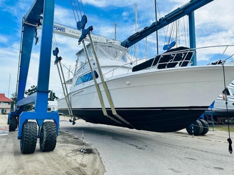 1988 Bertram 54' yacht being lifted by a boat hoist at a marina.