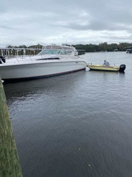 1993 Sea Ray 440 Sundancer docked beside a small yellow boat on a cloudy day.