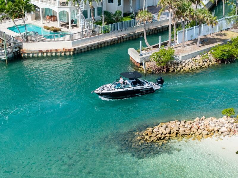 2023 Monterey 255 Super Sport boat cruising in a scenic coastal waterway near luxury homes.