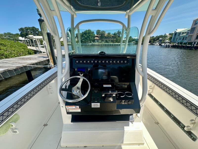 2019 Wellcraft 262 Fisherman boat console with steering wheel, docked by a scenic waterfront.