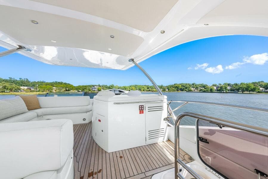 2016 Sunseeker Manhattan 65 yacht deck with seating, overlooking serene water and lush greenery.