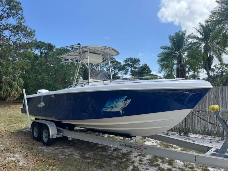 1998 Blue Fin 25 Center Console boat on trailer, featuring a fish graphic, surrounded by trees.