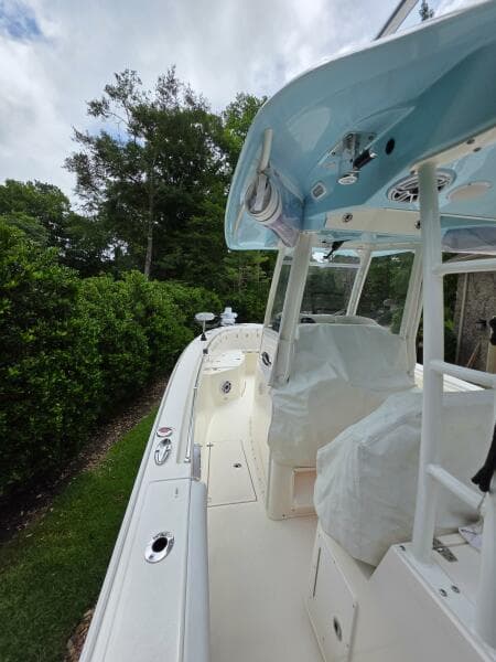 2021 Cobia 301 Center Console boat with covered seating, docked near lush greenery.