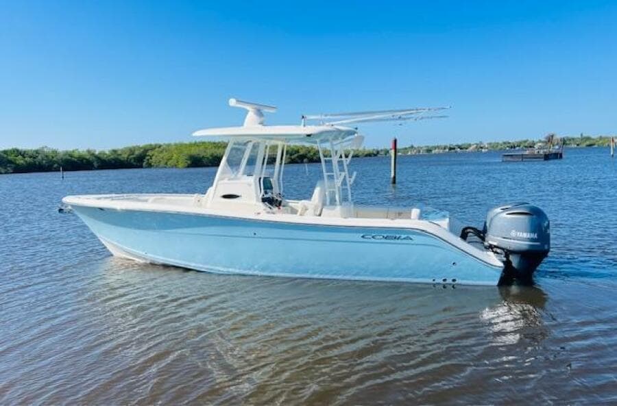 2021 Cobia 301 Center Console boat on calm water, clear blue sky background.